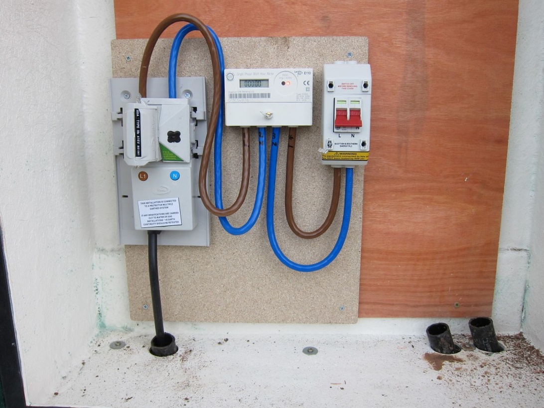 Professionellt installerad elcentral på en vägg, med elmätare, huvudbrytare och kopplingsdosa, vilket visar en färdig elinstallation.