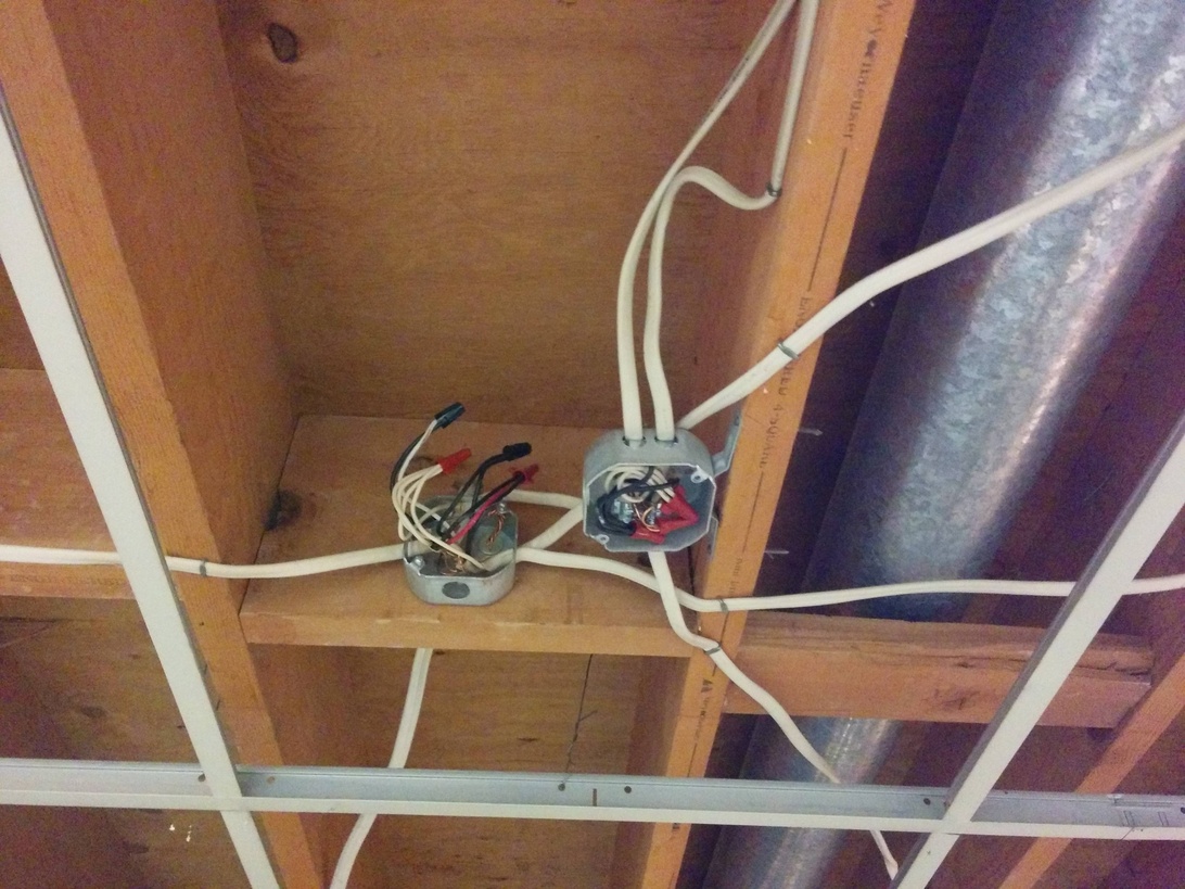 Närbild av elinstallation under byggnation, med synliga kopplingsdosor monterade på trästomme och elkablar dragna genom takbjälkar i ett oinrett tak.