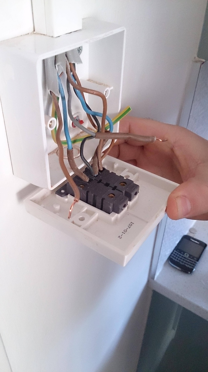 Närbild på en eluttagsinstallation där en persons hand ansluter olikfärgade ledningar till en kopplingsdosa.
